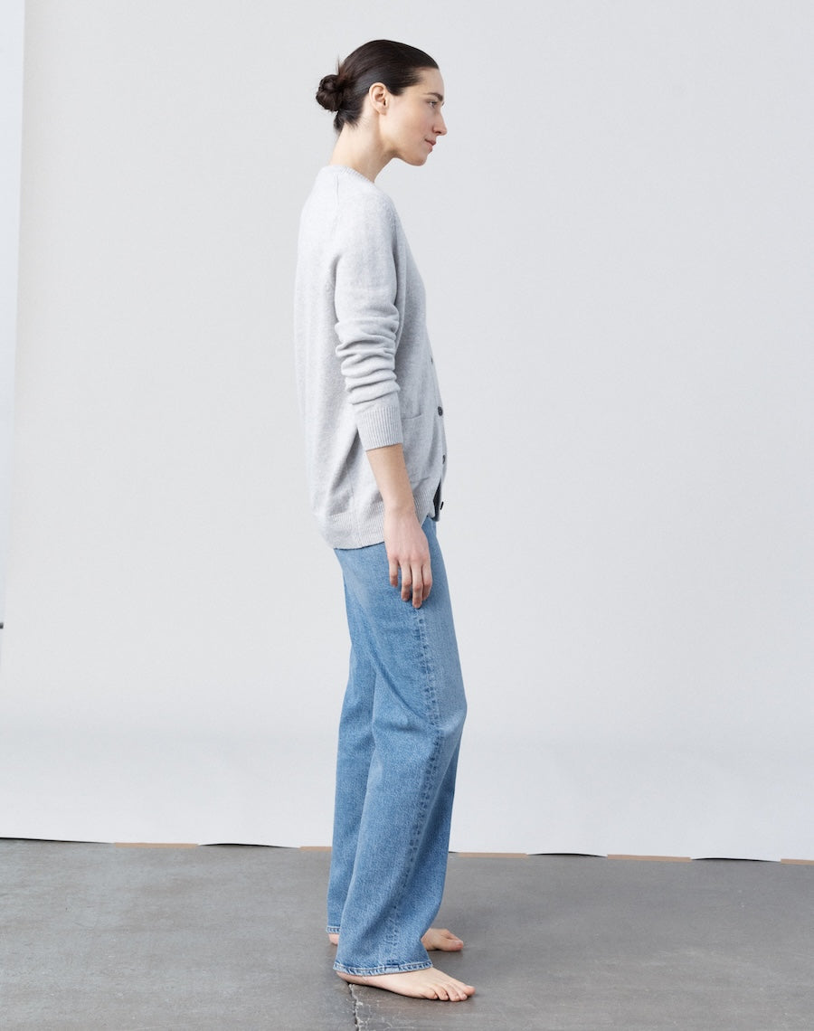 Person wearing a gray sweater and blue jeans standing against a white wall.